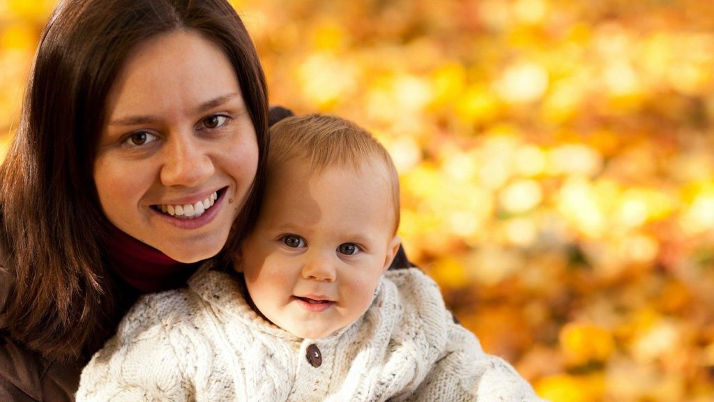 落ち葉を背景に笑顔で笑うお母さんと赤ちゃんの写真