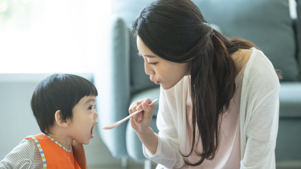 赤ちゃんに離乳食をあげながら声掛けをするお母さんの写真